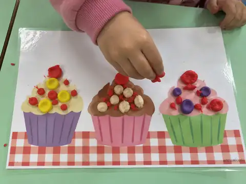 Niña decorando cupcakes con plastilina en el tapete